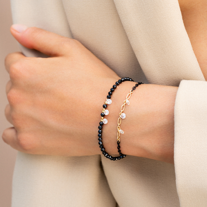 Bracciale elastico GIPSY CHIC con zirconi milky neri e tre zirconi bianchi pendenti al centro indossato insieme ad un'altro bracciale della stessa collezione Rue des Mille.