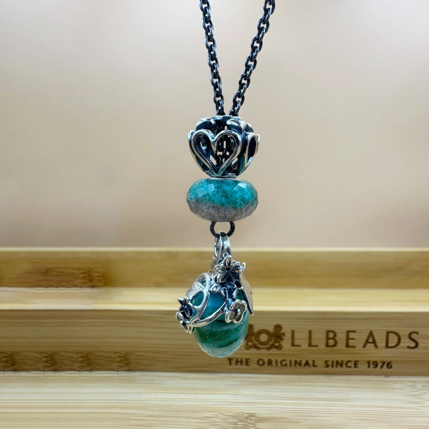 Collana Fresco Bagliore. Collana composta da: beads sfaccettato turchese e azzurrro ghiaccio, pendente con montatura floreale in argento e vetro sfaccettato con pallete di colori: verde acqua, verde smeraldo tenue e turchese, beads "Sempre Insieme" in argento con cuoricini traforati | Golden Party Trollbeads