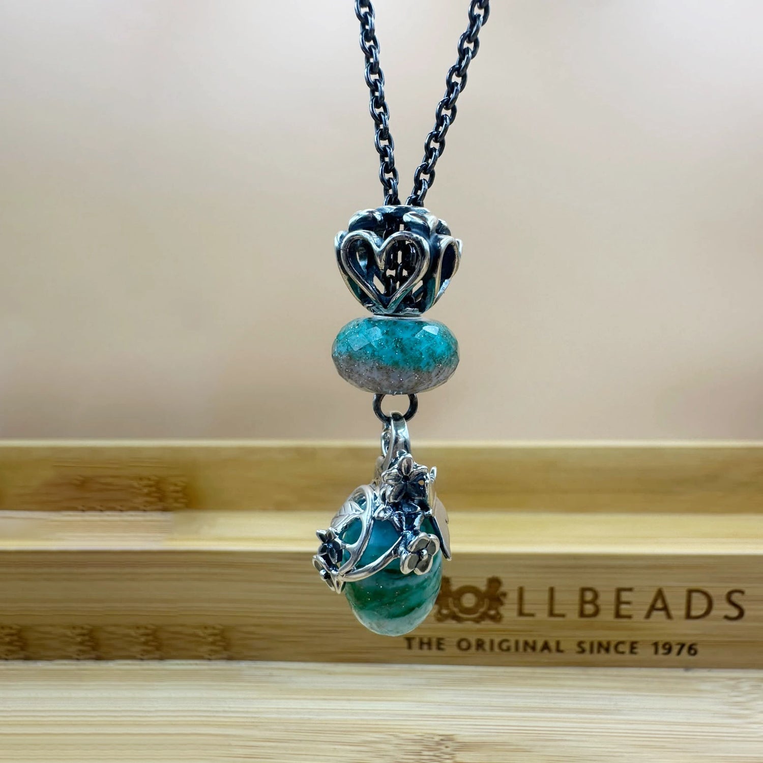 Collana Fresco Bagliore. Collana composta da: beads sfaccettato turchese e azzurrro ghiaccio, pendente con montatura floreale in argento e vetro sfaccettato con pallete di colori: verde acqua, verde smeraldo tenue e turchese, beads "Sempre Insieme" in argento con cuoricini traforati | Golden Party Trollbeads